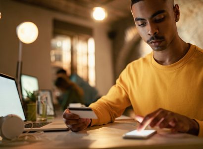 African American businessman using credit cart and mobile phone while checking his online bank account during late night work in the office.