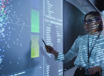 Young Female Teacher Giving a Data Science Presentation in a Dark Auditorium with Projecting Slideshow with Artificial Intelligence Neural Network Architecture. Business Startup and Education Concept